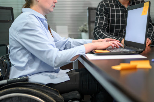 A man in a wheelchair tying on a computer.