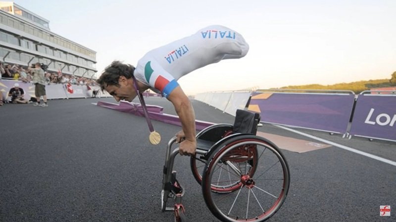 Alex Zanardi on a racetrack performing a handstand on the bars of his wheelchair
