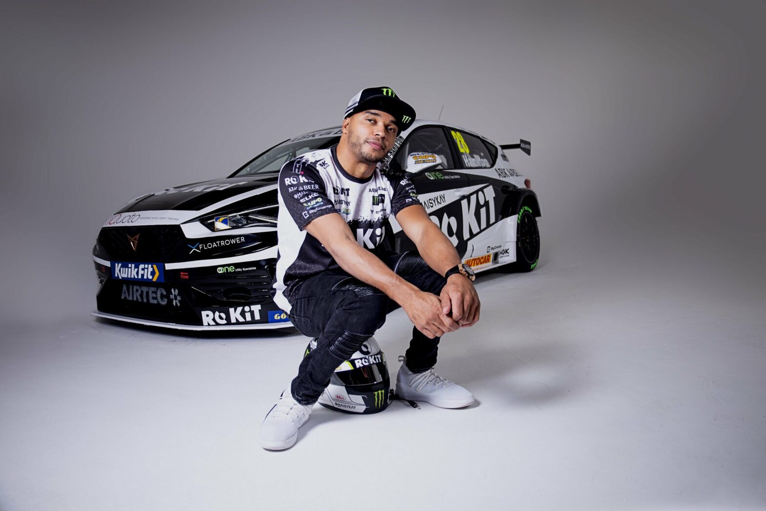 Nicolas Hamilton sitting on a helmet in front of a parked sportscar