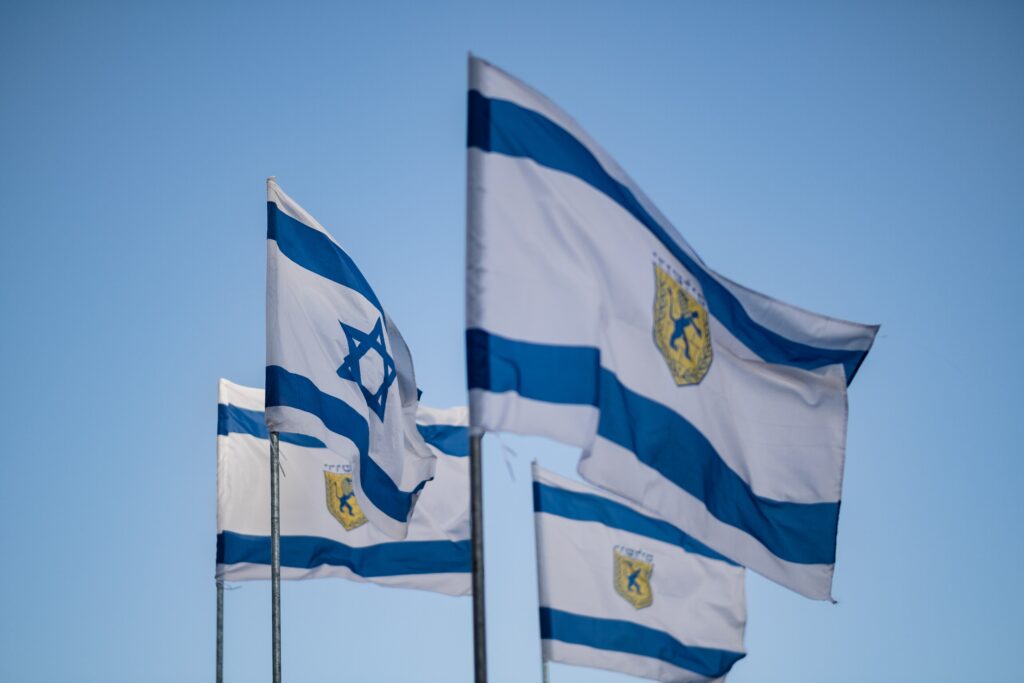 The Israeli Flag which depicts the depicts a blue hexagram on a white background, between two horizontal blue stripes.