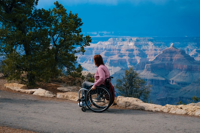 A woman in a wheelchair enjoying a scenic view of the mountains from a side-road.